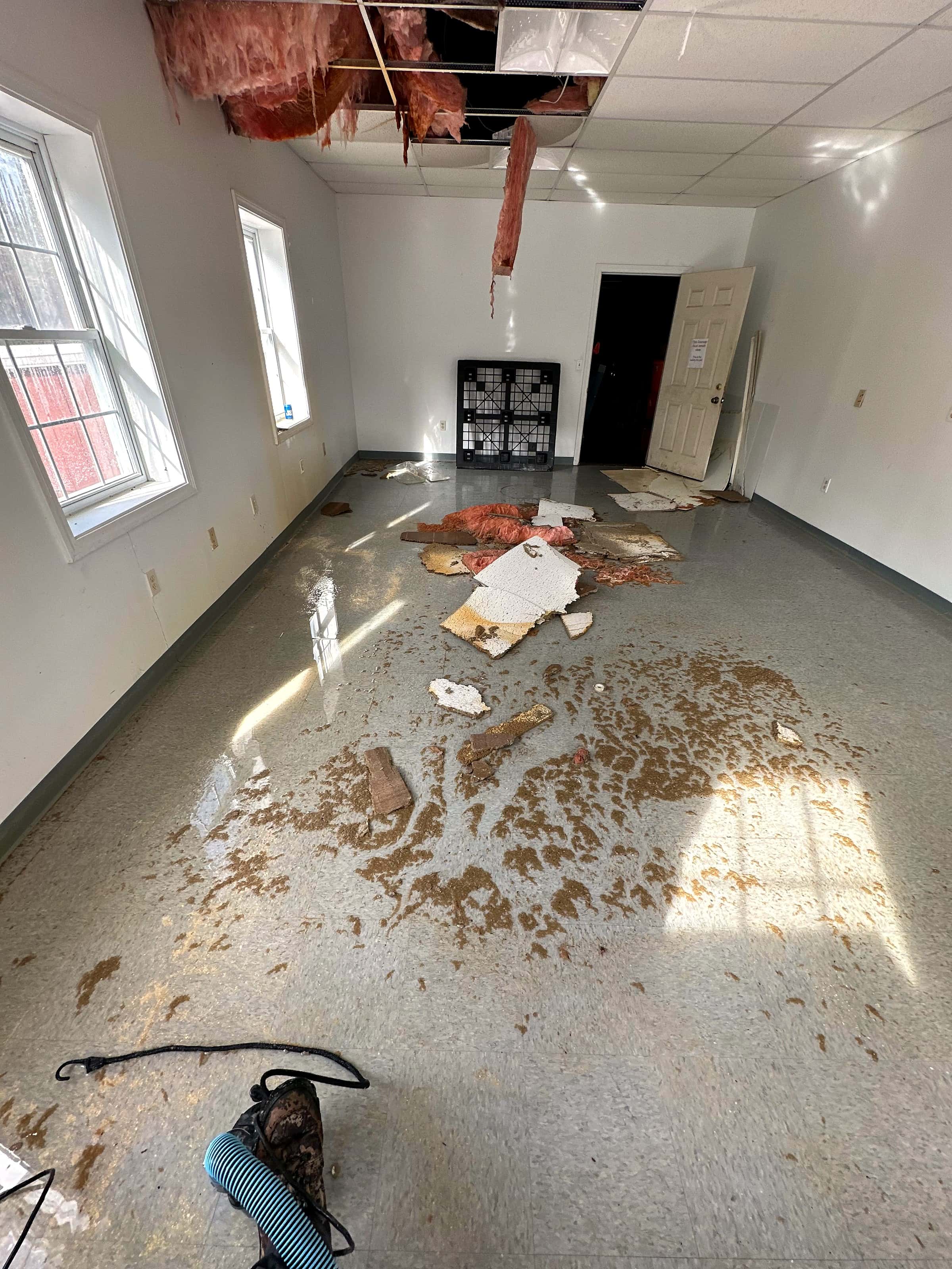 A collapsed ceiling with wet insulation and debris across the floor of an office.