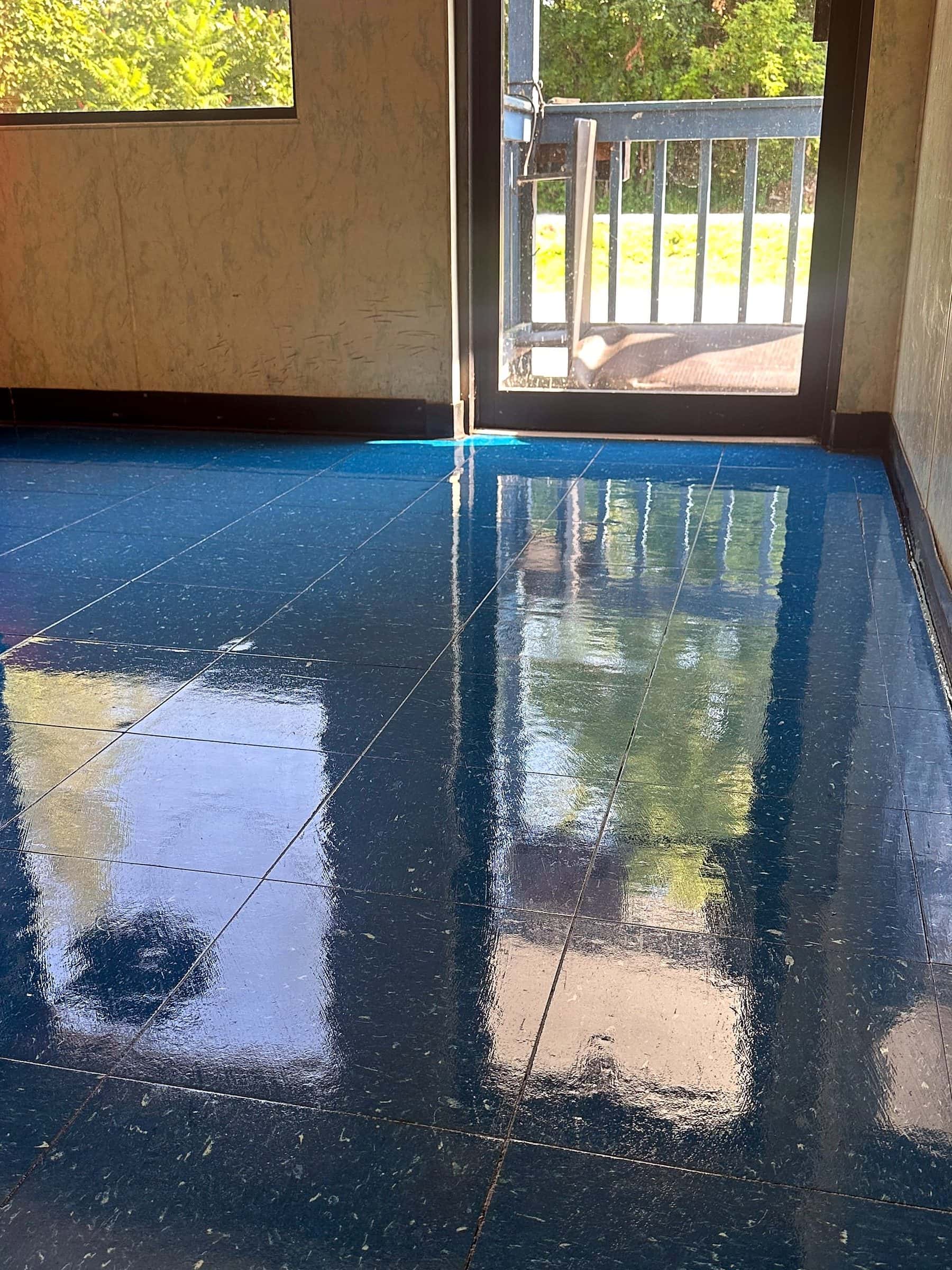 An entrance floor of blue tile after strip and wax, the finish reflecting the glass door and the window.