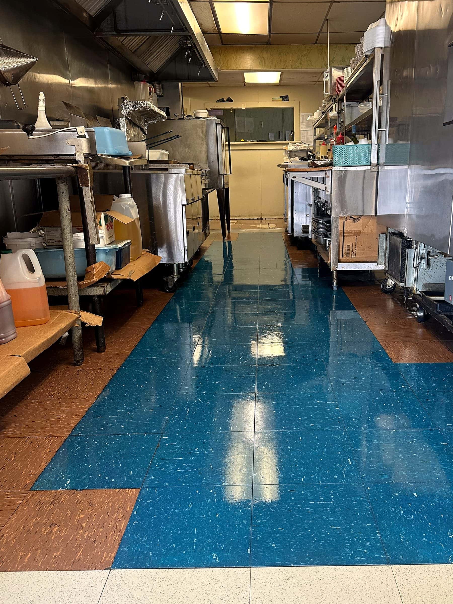 The same kitchen aisle after strip and wax, the blue tile reflecting the ceiling lights.