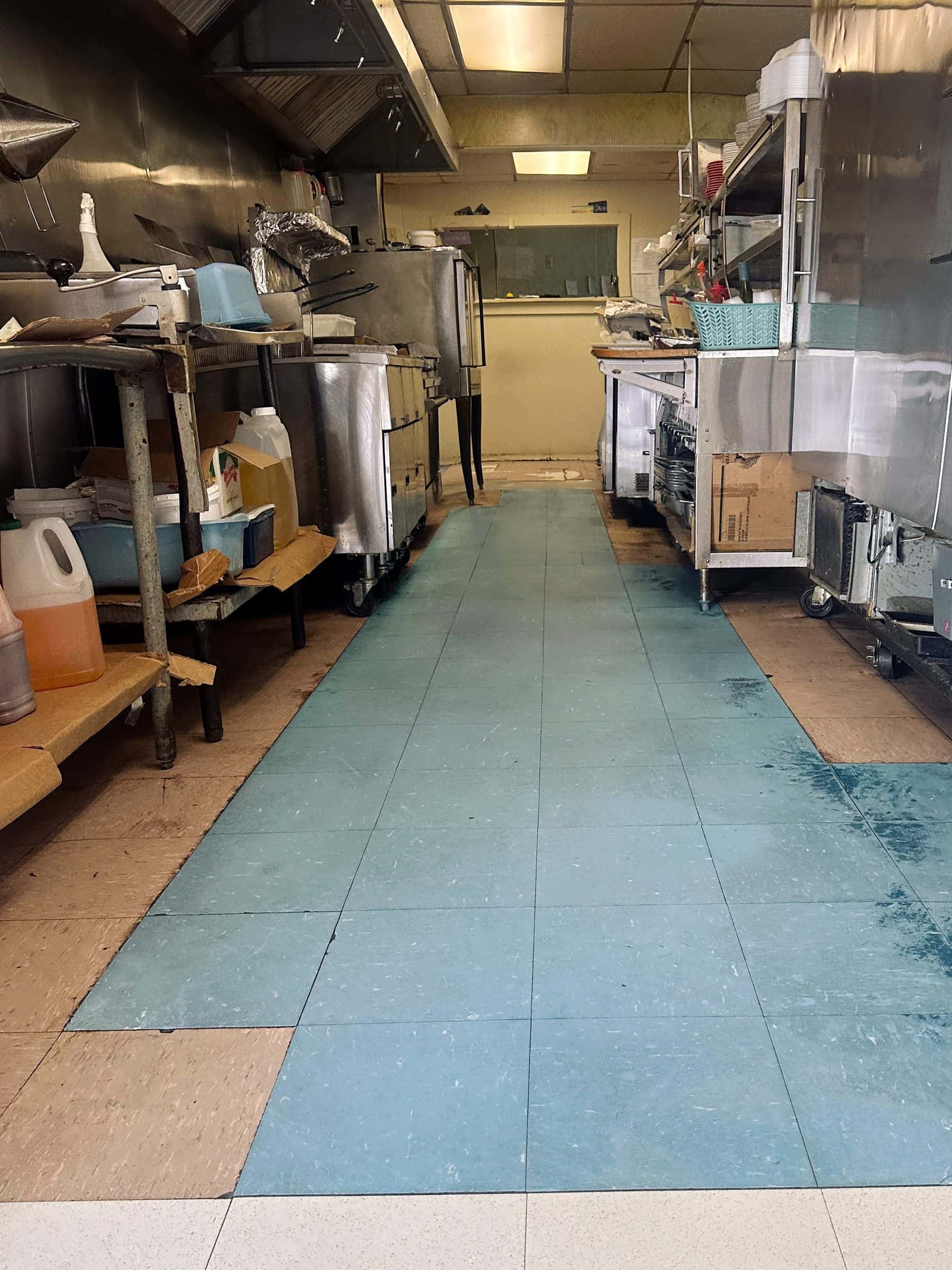 The aisle of a commercial kitchen with a worn, dull tile floor before it was stripped and refinished.