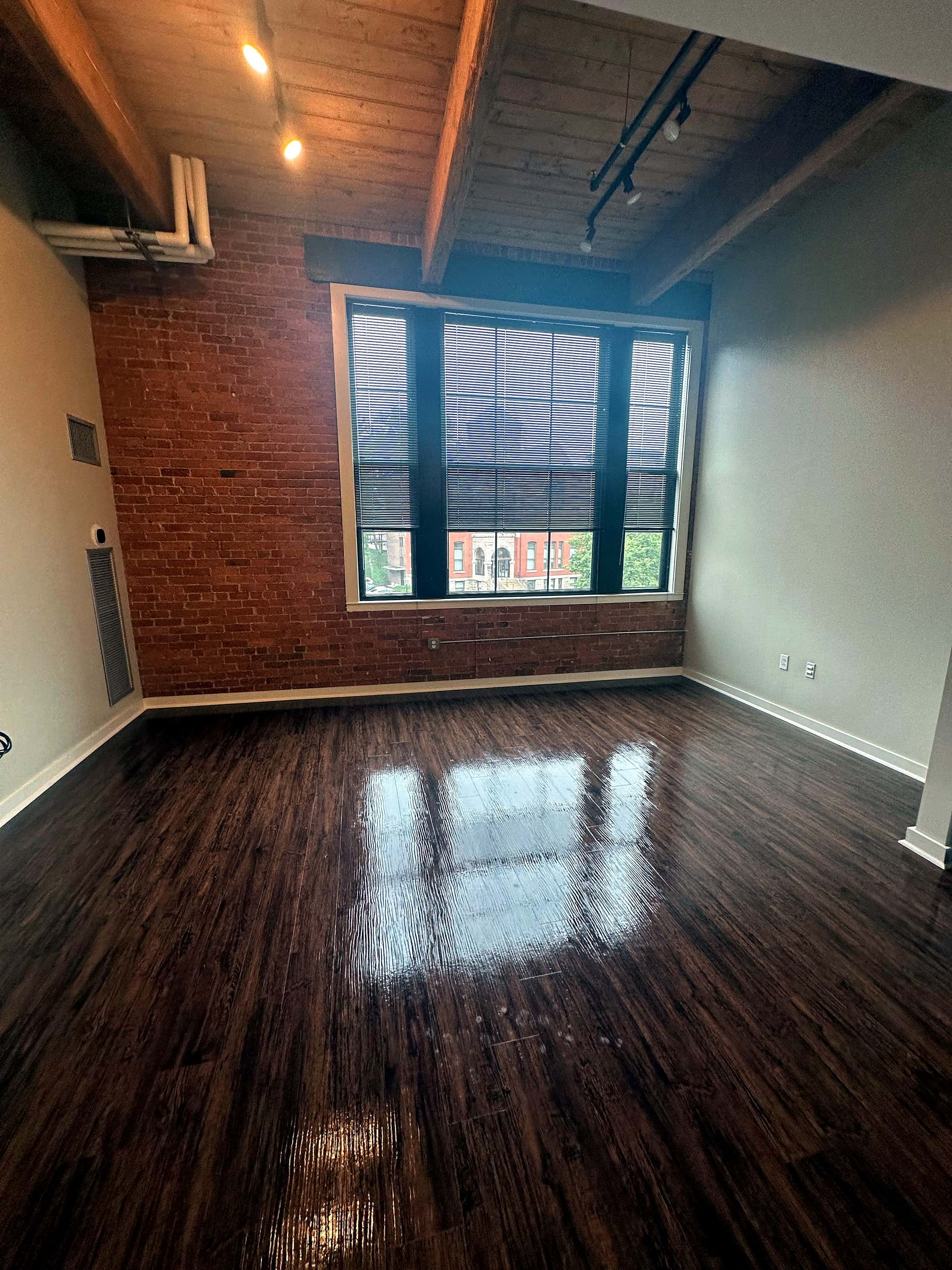 A finished office room with a refinished wood floor, a brick wall and a tall window.
