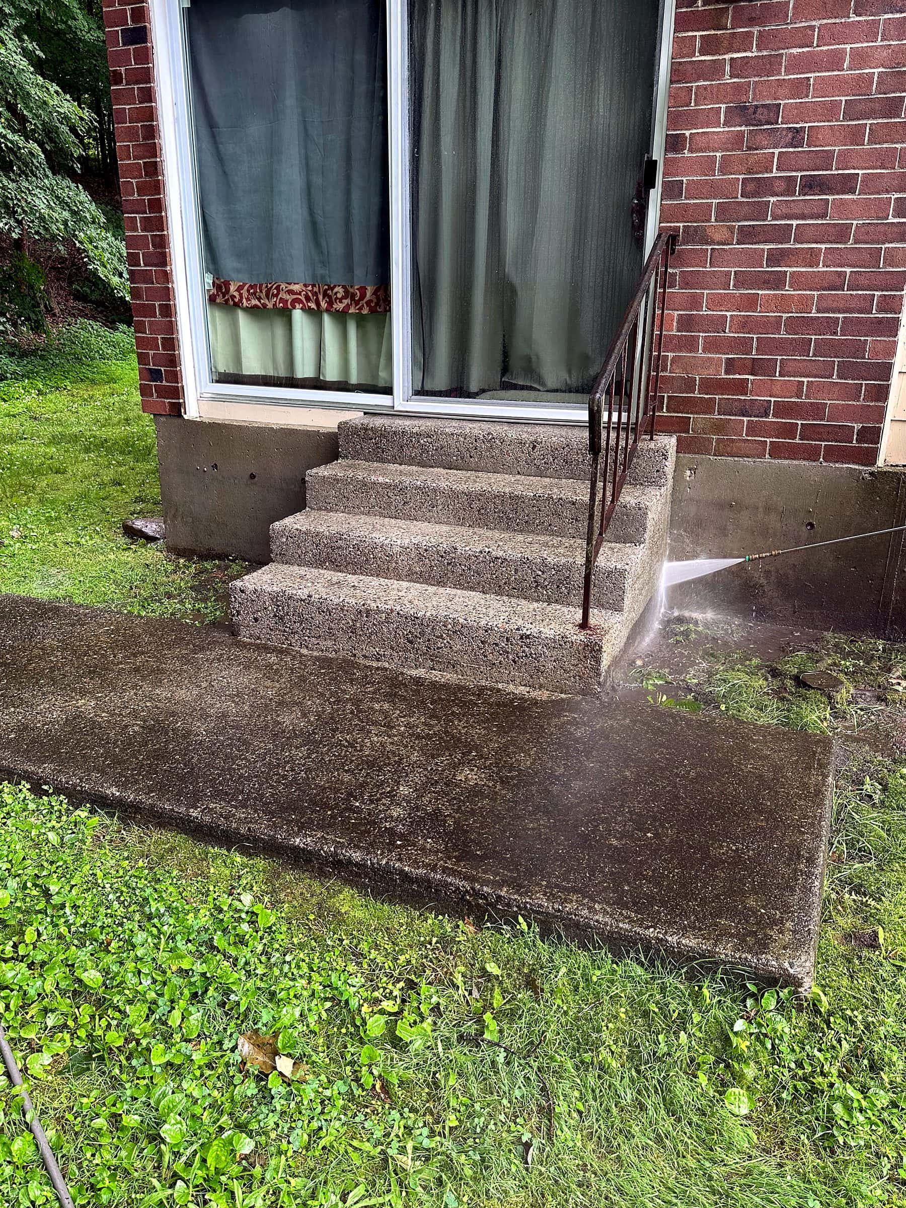 A pressure washer jet cleaning concrete steps and a walkway outside a brick building.
