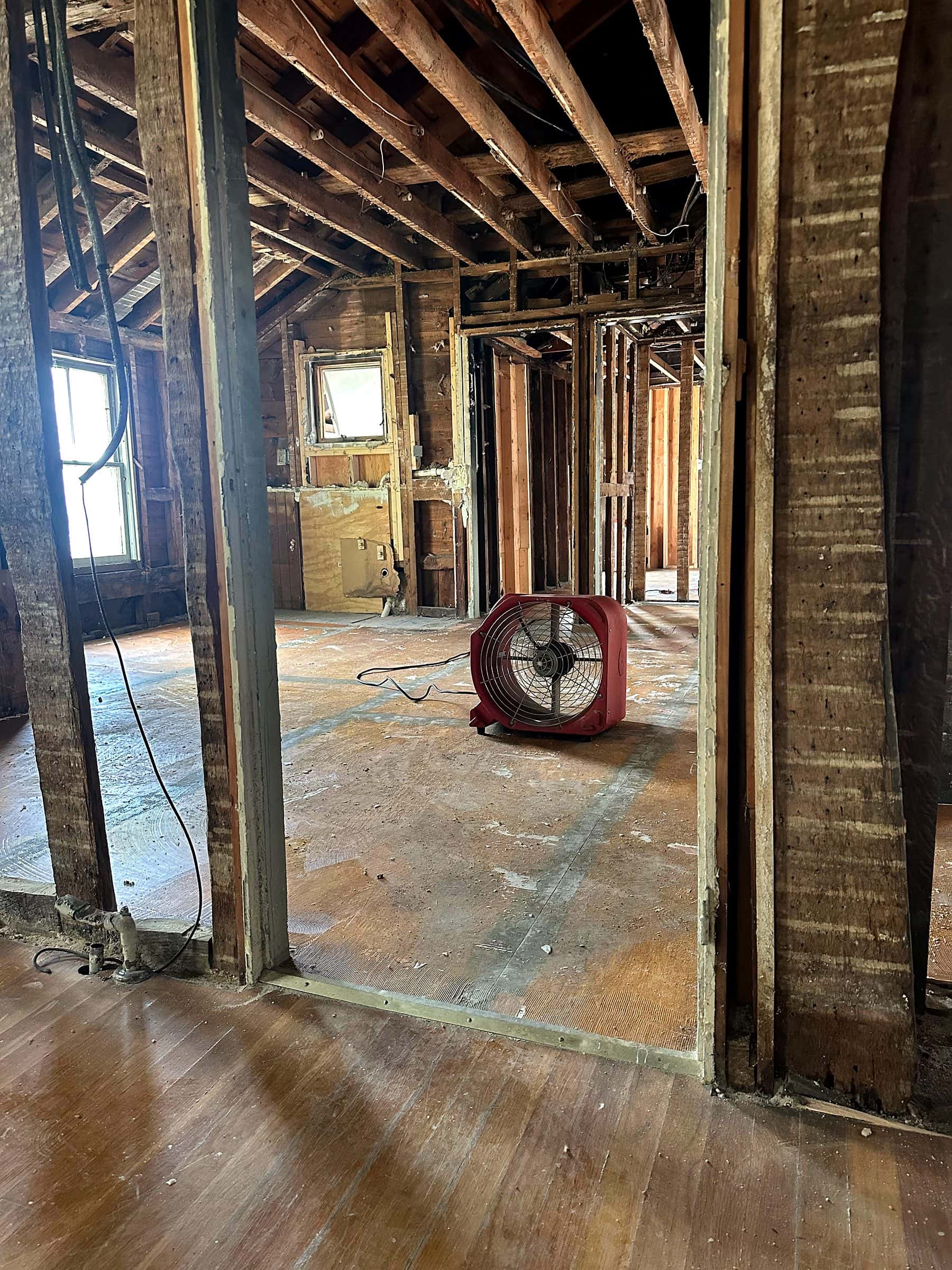 A framed doorway between old and new wall studs in a gutted building, with an air mover on the subfloor.